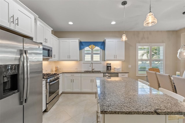 kitchen with white cabinetry, sink, stainless steel appliances, decorative light fixtures, and stone countertops