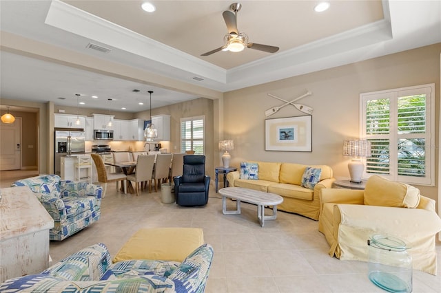 living room with ceiling fan, a healthy amount of sunlight, ornamental molding, and a tray ceiling