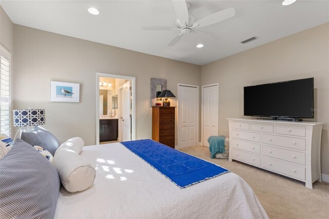 bedroom featuring ceiling fan, light carpet, connected bathroom, and two closets