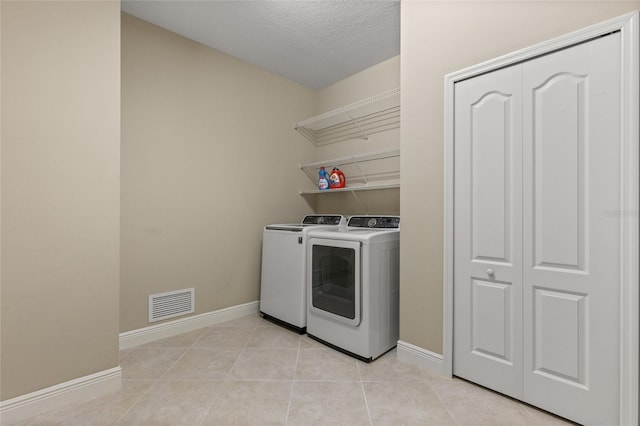 laundry room with light tile patterned floors, washer and dryer, and a textured ceiling