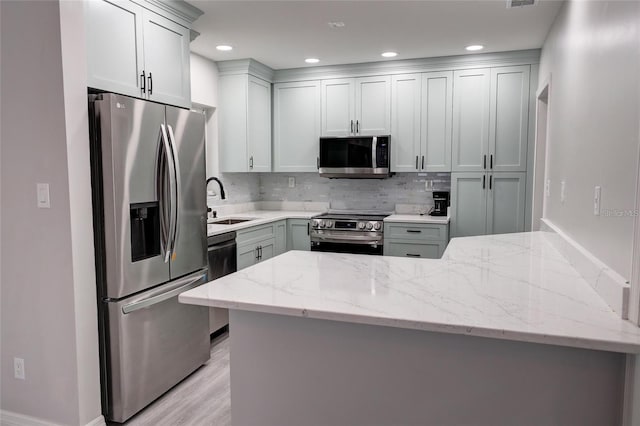 kitchen featuring decorative backsplash, appliances with stainless steel finishes, light wood-type flooring, kitchen peninsula, and light stone counters