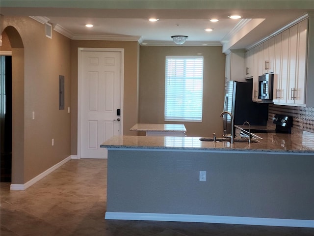 kitchen with kitchen peninsula, appliances with stainless steel finishes, light stone countertops, sink, and white cabinetry