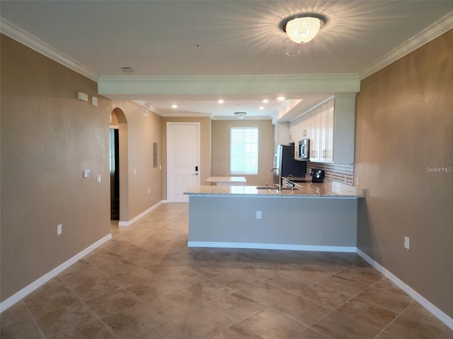 kitchen featuring stainless steel appliances, light stone counters, kitchen peninsula, white cabinets, and ornamental molding