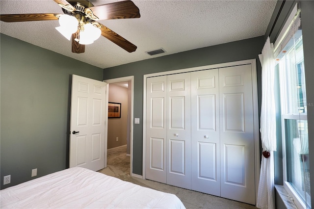 bedroom with a textured ceiling, ceiling fan, light colored carpet, visible vents, and a closet