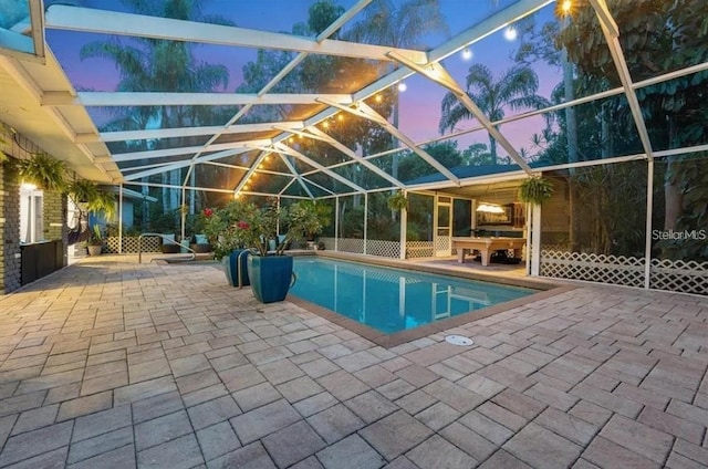 pool at dusk with a lanai and a patio area