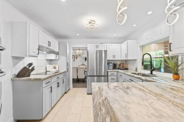 kitchen with light stone countertops, stainless steel fridge, black electric stovetop, sink, and white cabinetry