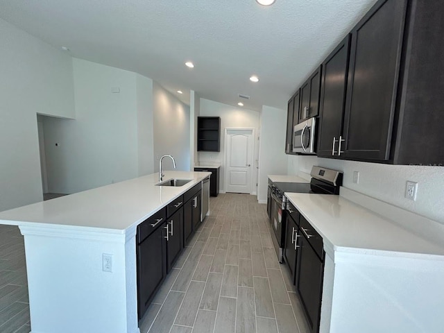 kitchen featuring stainless steel appliances, light countertops, a kitchen island with sink, a sink, and dark cabinetry