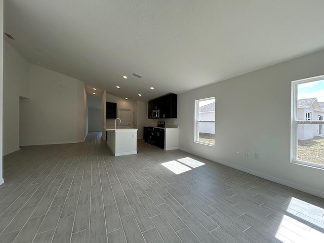 unfurnished living room featuring light wood finished floors, visible vents, vaulted ceiling, a sink, and baseboards