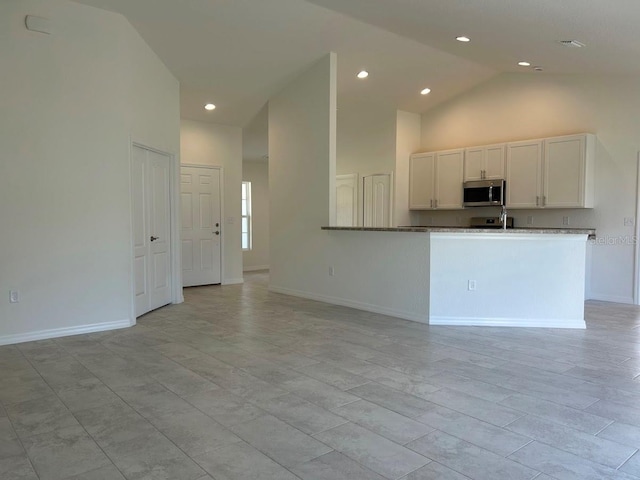 kitchen with stainless steel microwave, white cabinetry, high vaulted ceiling, a peninsula, and baseboards