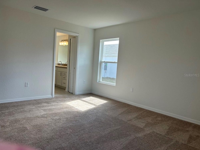 unfurnished bedroom featuring light carpet, ensuite bathroom, visible vents, and baseboards