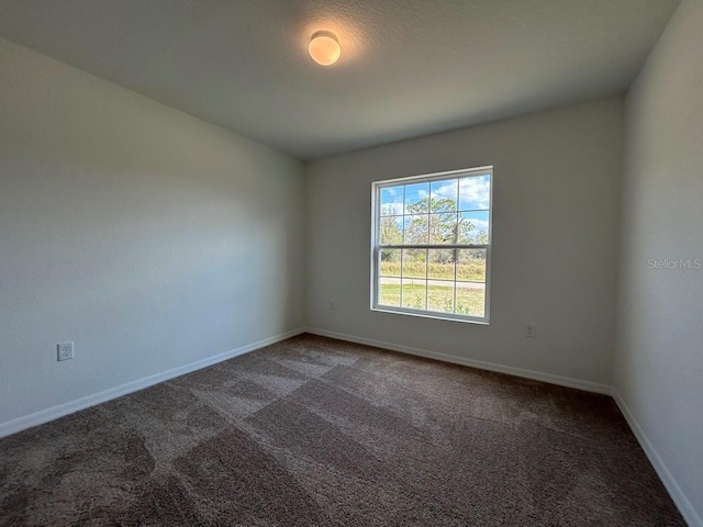 spare room featuring dark colored carpet and baseboards