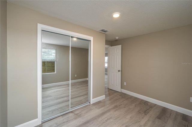 unfurnished bedroom featuring a closet, a textured ceiling, and light hardwood / wood-style flooring