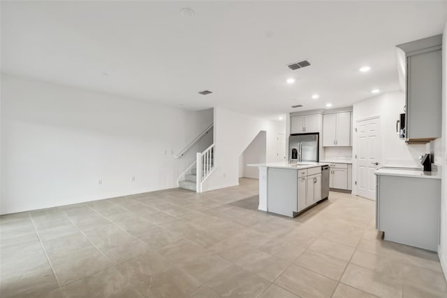 kitchen with light tile patterned floors, sink, appliances with stainless steel finishes, and an island with sink