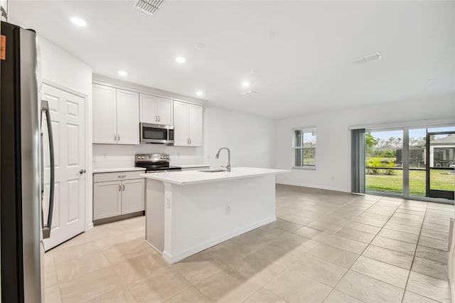 kitchen with light tile patterned floors, white cabinetry, stainless steel appliances, and a center island with sink