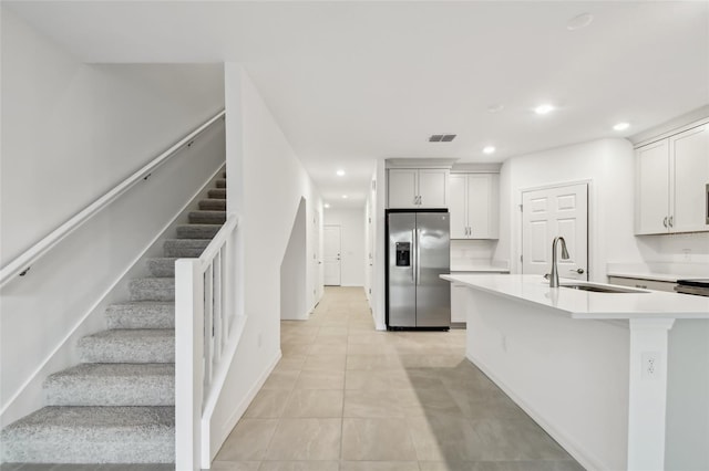 kitchen featuring stainless steel fridge with ice dispenser, a center island with sink, a kitchen breakfast bar, white cabinets, and sink