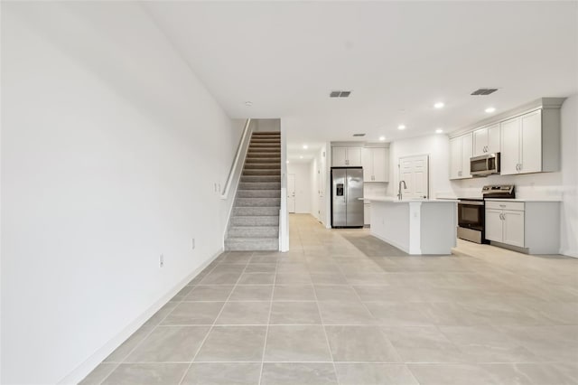 kitchen with light tile patterned floors, sink, appliances with stainless steel finishes, and an island with sink