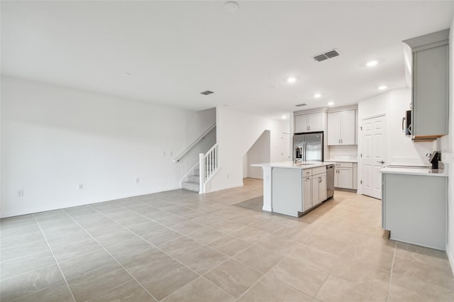 kitchen with light tile patterned floors, appliances with stainless steel finishes, and a kitchen island with sink