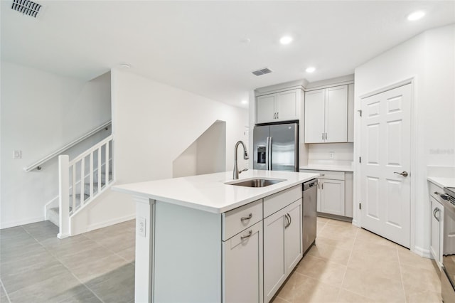 kitchen featuring appliances with stainless steel finishes, gray cabinetry, sink, light tile patterned floors, and a center island with sink