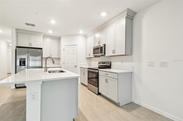 kitchen with a center island with sink, sink, gray cabinetry, stainless steel appliances, and light tile patterned floors