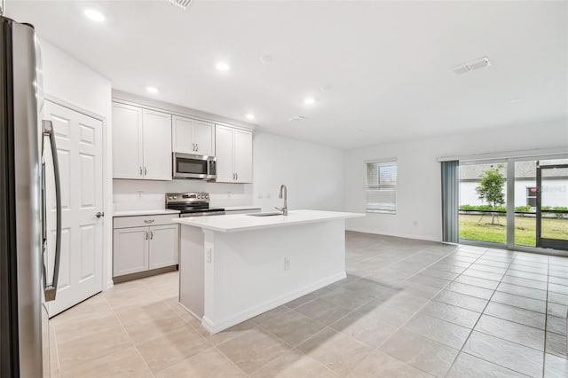 kitchen with appliances with stainless steel finishes, white cabinetry, sink, a kitchen island with sink, and light tile patterned flooring