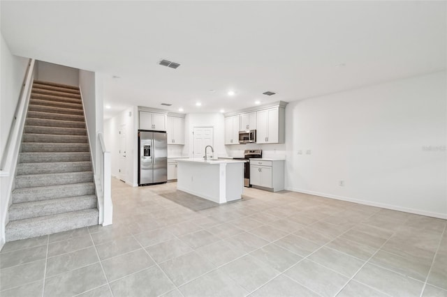 kitchen with appliances with stainless steel finishes, white cabinetry, an island with sink, sink, and light tile patterned flooring