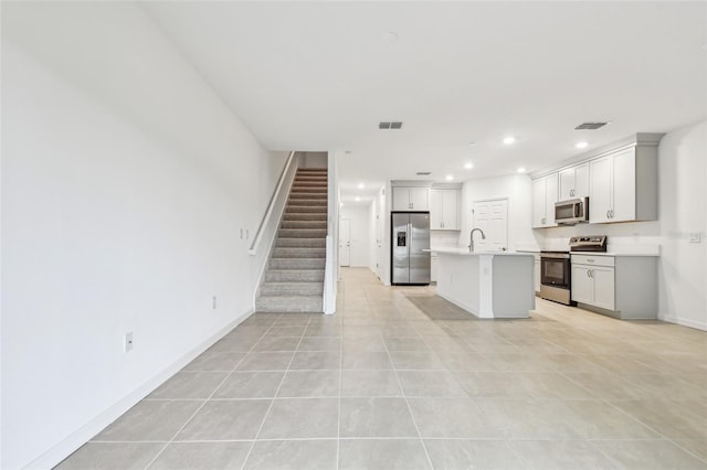 kitchen featuring sink, light tile patterned floors, stainless steel appliances, and a kitchen island with sink