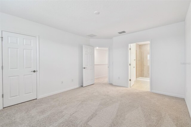 unfurnished bedroom with light carpet, a closet, and connected bathroom