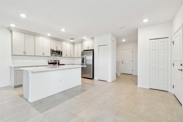 kitchen with a center island with sink, sink, light tile patterned floors, appliances with stainless steel finishes, and white cabinets