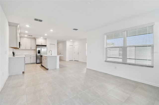 kitchen with light tile patterned floors, white cabinets, appliances with stainless steel finishes, and a center island with sink