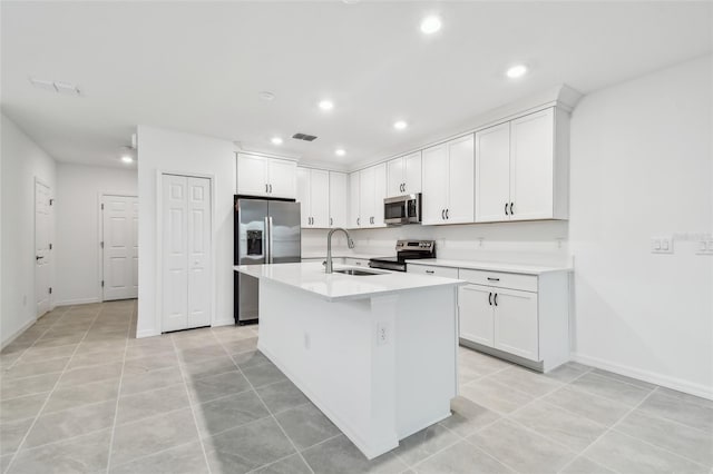 kitchen featuring sink, light tile patterned floors, appliances with stainless steel finishes, an island with sink, and white cabinets