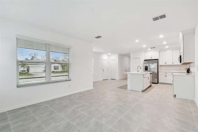 kitchen with white cabinetry, an island with sink, sink, stainless steel fridge, and light tile patterned floors