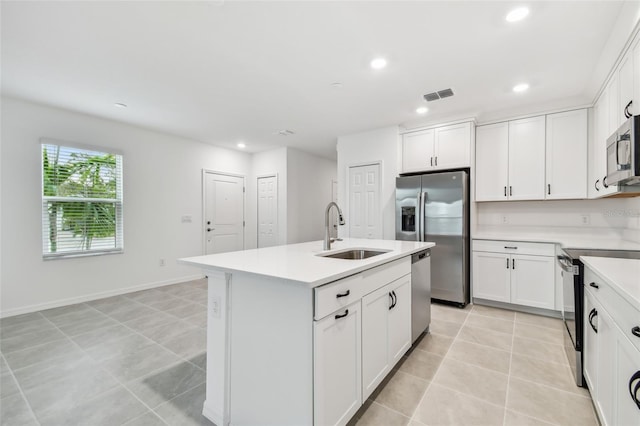 kitchen with white cabinetry, stainless steel appliances, sink, a kitchen island with sink, and light tile patterned flooring