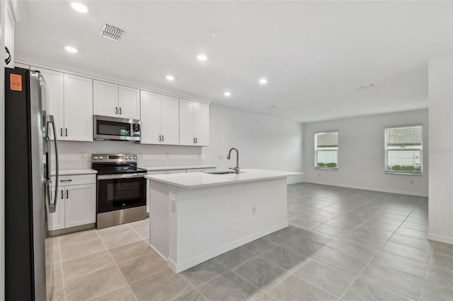 kitchen featuring white cabinets, stainless steel appliances, sink, light tile patterned floors, and a center island with sink