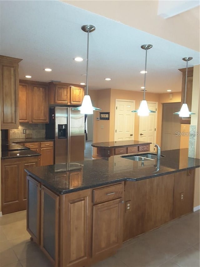 kitchen with stainless steel refrigerator with ice dispenser, sink, light tile patterned floors, pendant lighting, and dark stone countertops