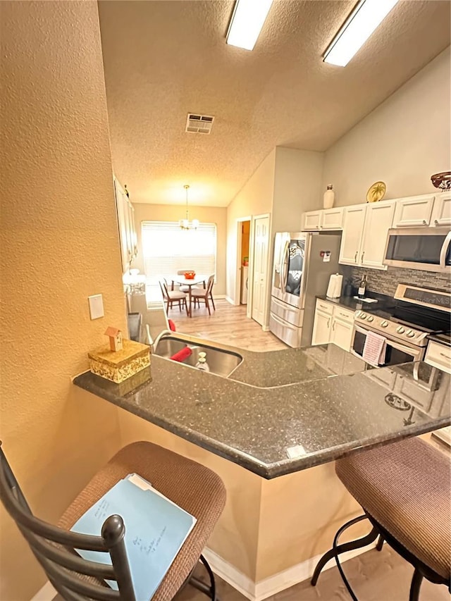 kitchen with a breakfast bar, kitchen peninsula, a textured ceiling, appliances with stainless steel finishes, and white cabinetry