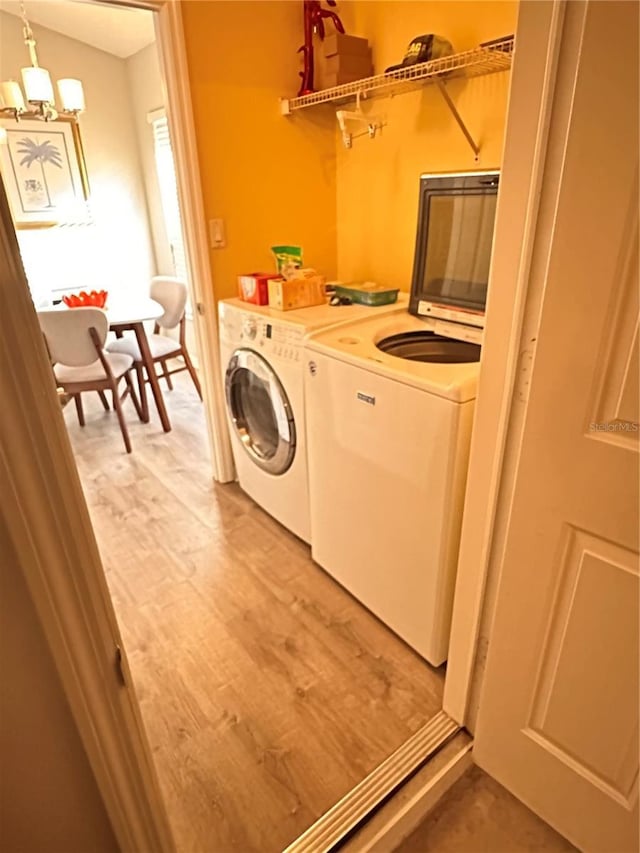 clothes washing area featuring hardwood / wood-style flooring, washer and clothes dryer, and a notable chandelier