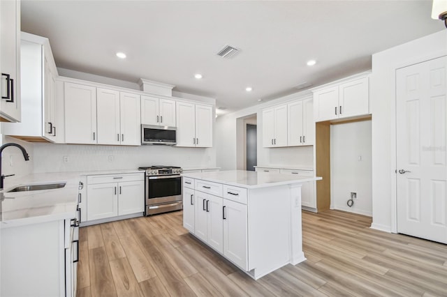 kitchen with light wood-type flooring, stainless steel appliances, sink, white cabinets, and a center island