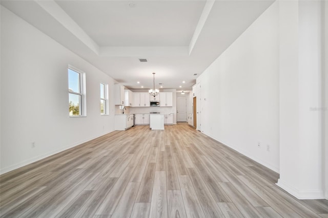 unfurnished living room featuring a notable chandelier, light hardwood / wood-style floors, a raised ceiling, and sink