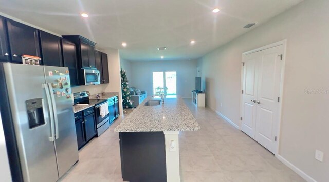 kitchen featuring sink, light stone counters, a kitchen island with sink, light tile patterned floors, and appliances with stainless steel finishes