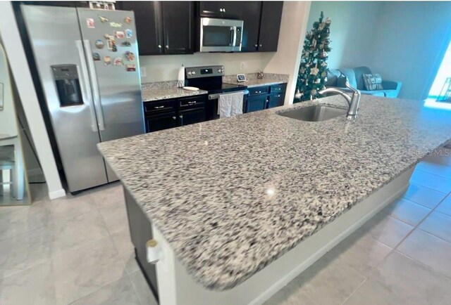 kitchen with light stone countertops, sink, a kitchen island with sink, and appliances with stainless steel finishes