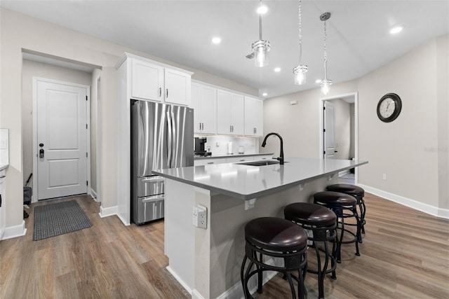 kitchen featuring stainless steel fridge, sink, a center island with sink, white cabinetry, and hanging light fixtures