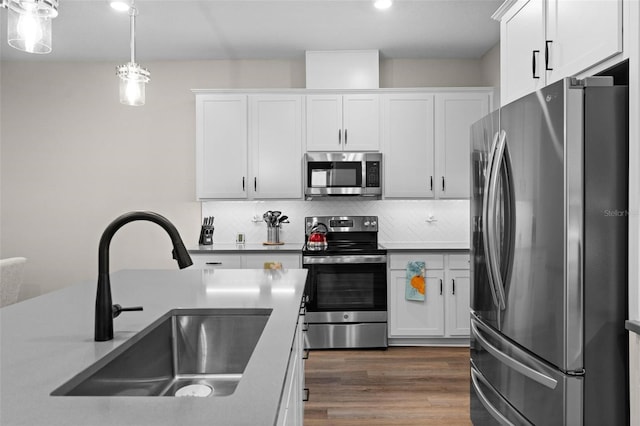 kitchen with sink, stainless steel appliances, pendant lighting, decorative backsplash, and white cabinets