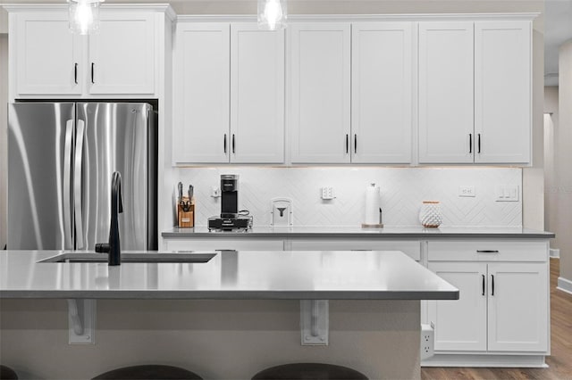 kitchen with stainless steel refrigerator, a breakfast bar area, decorative backsplash, white cabinets, and light wood-type flooring