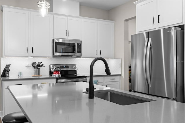 kitchen featuring tasteful backsplash, stainless steel appliances, sink, decorative light fixtures, and white cabinetry