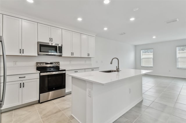 kitchen with stainless steel appliances, white cabinetry, sink, and a center island with sink