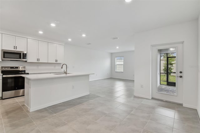 kitchen with sink, a center island with sink, light tile patterned floors, stainless steel appliances, and white cabinets