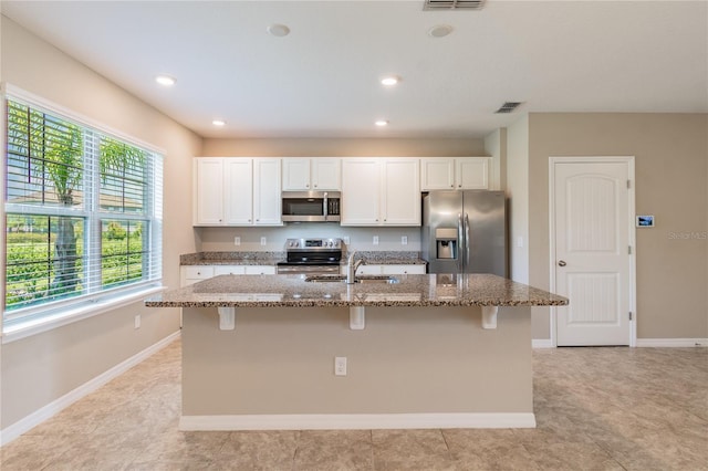 kitchen featuring sink, stone counters, an island with sink, and appliances with stainless steel finishes