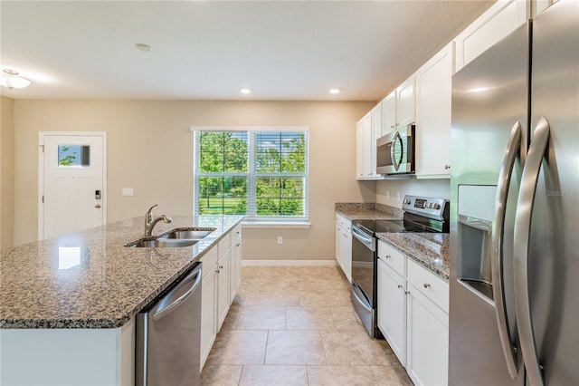 kitchen with white cabinets, stainless steel appliances, an island with sink, stone counters, and sink