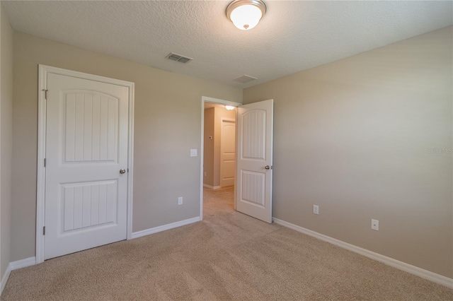 unfurnished bedroom featuring a textured ceiling, a closet, and light carpet