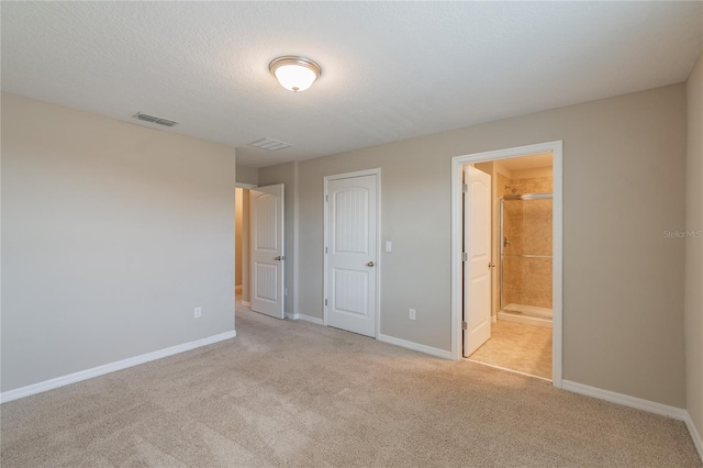 unfurnished bedroom with a textured ceiling, light colored carpet, ensuite bathroom, and a closet